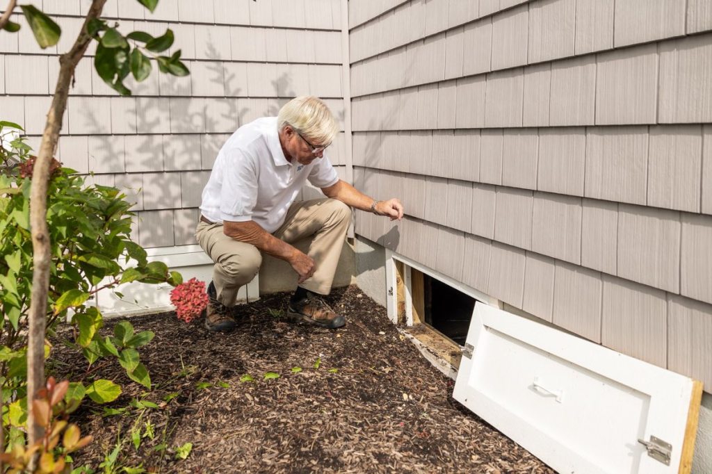 A property inspector checking an exterior crawlspace entrance beside a home